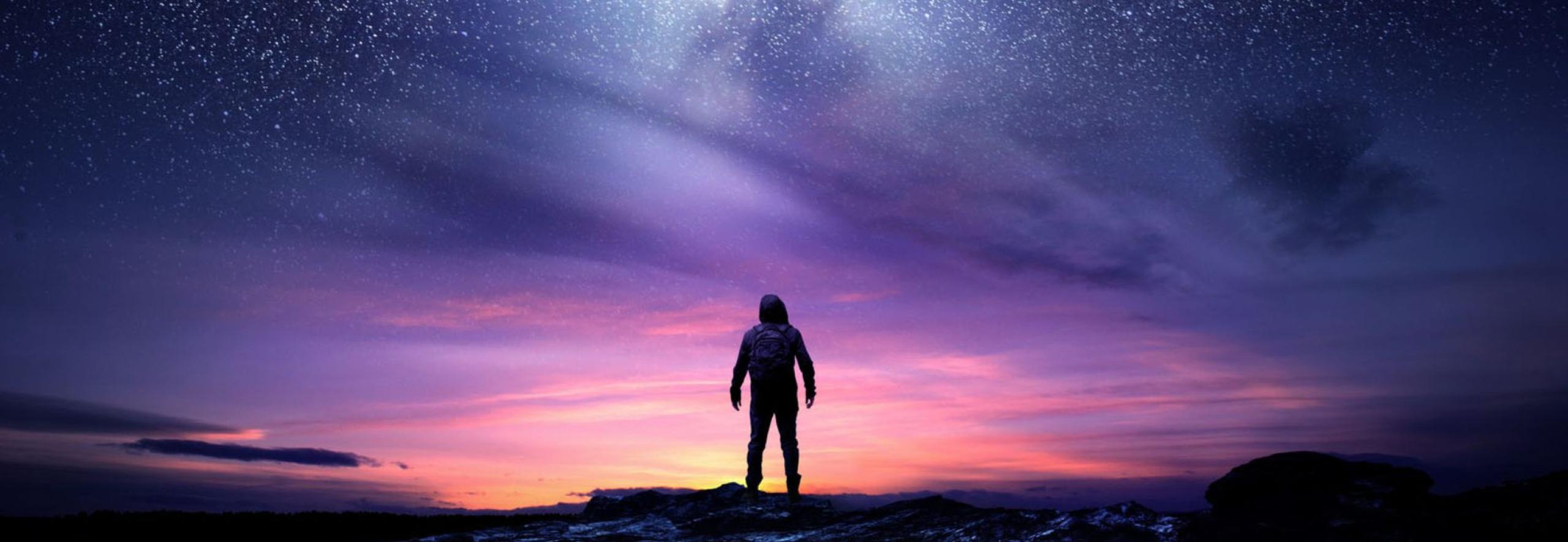 Person standing on rocks gazing up at starry sky